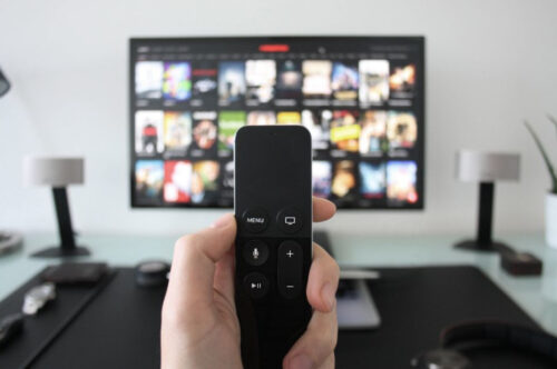 person holding remote in front of tv that is turned on