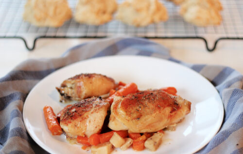 Plated chicken thighs with carrots and parsnips, biscuits in the background