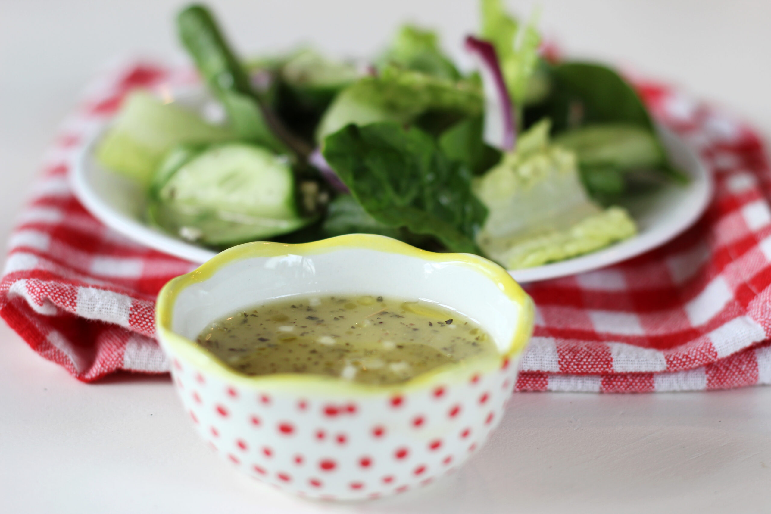 Bowl of lemon garlic salad dressing next to plate of salad