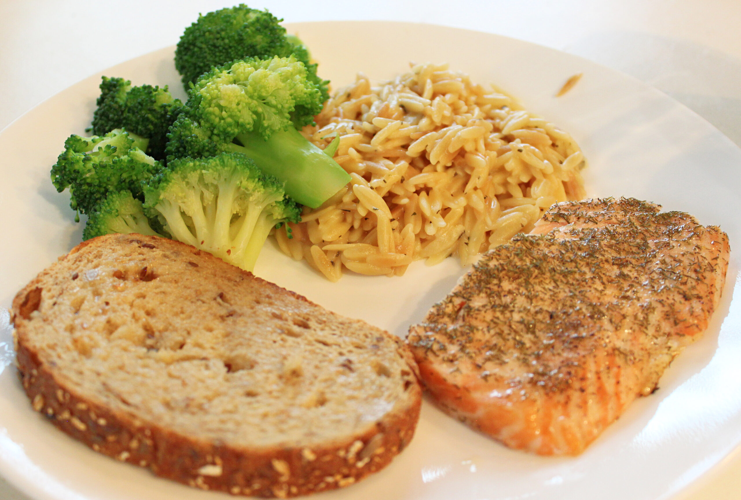 Plate of salmon, orzo, broccoli and a slice of whole grain bread